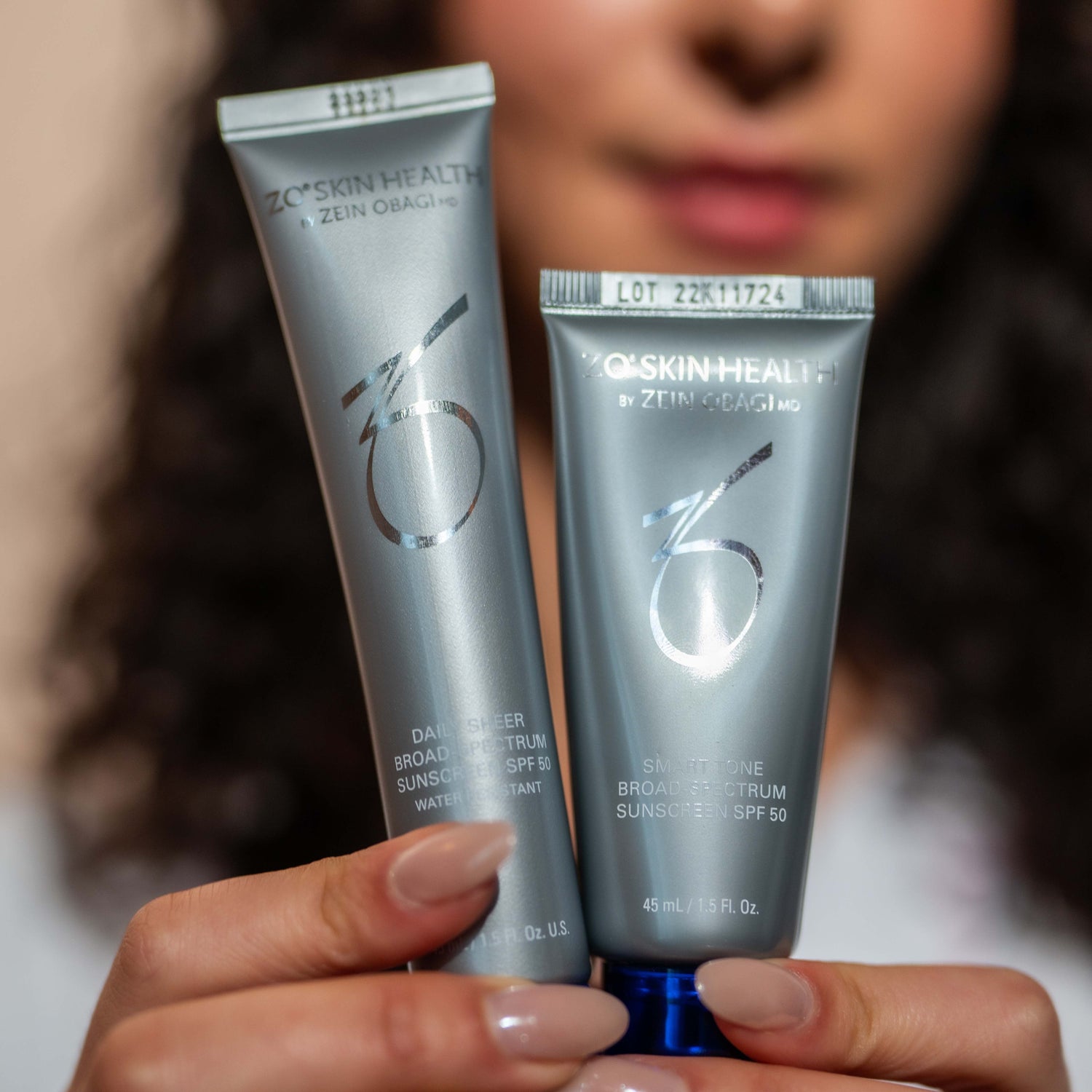 Kvinne med sol i ansiktet som holder opp to solkremer fra ZO Skin Health foran seg